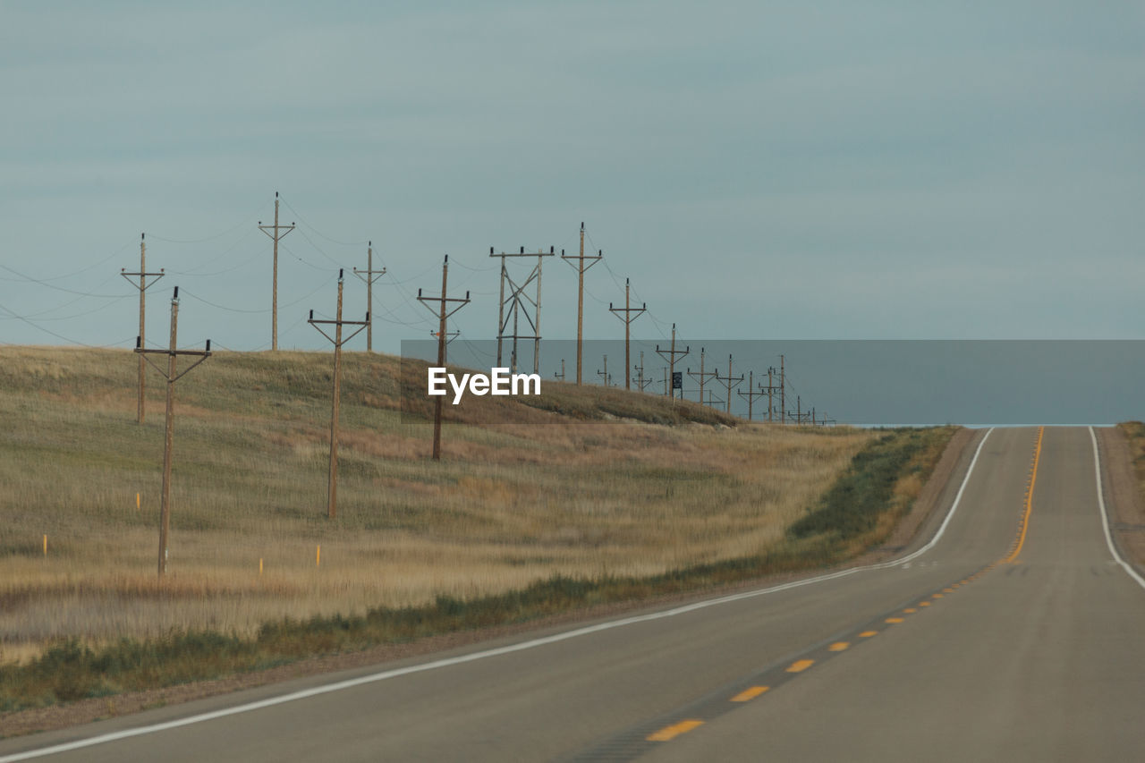 Road by electricity pylon against sky