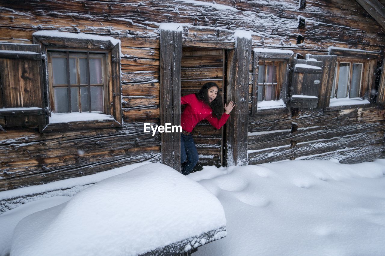 Portrait of shocked woman standing at snow covered entrance of house