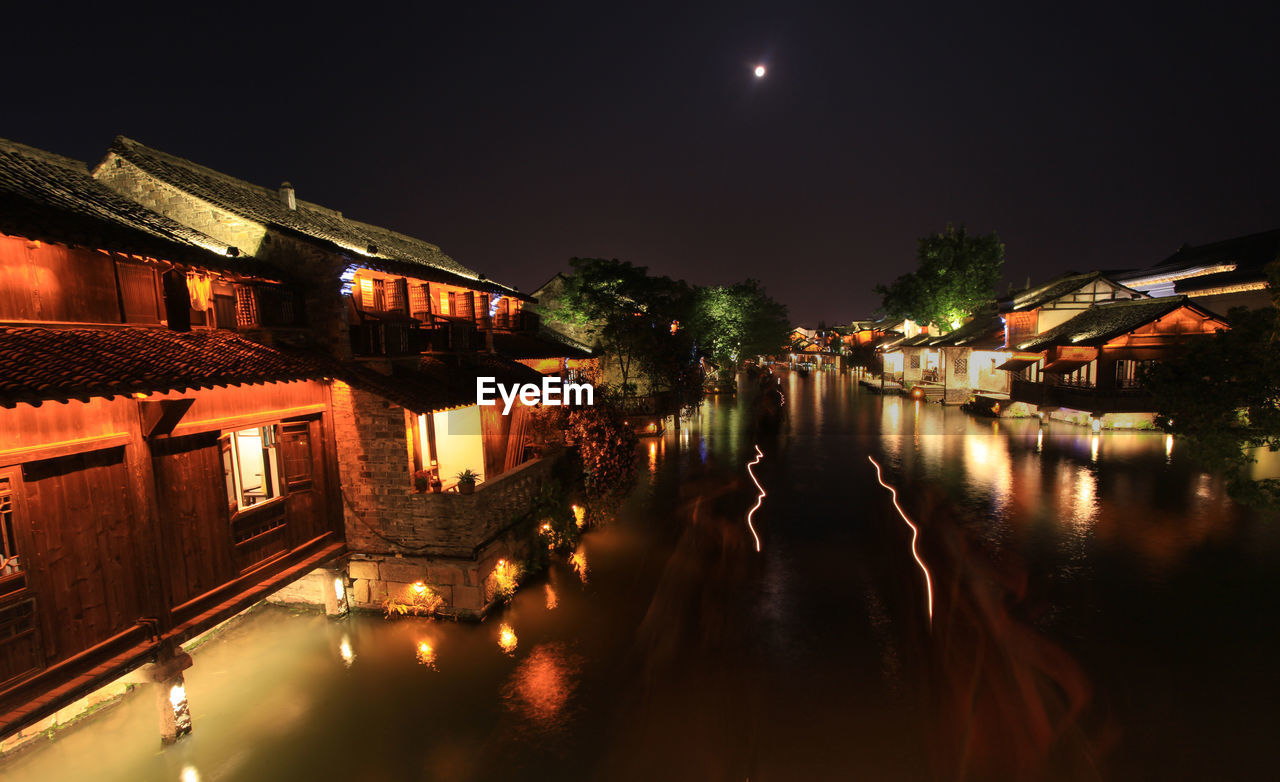 River amidst illuminated houses against sky at night