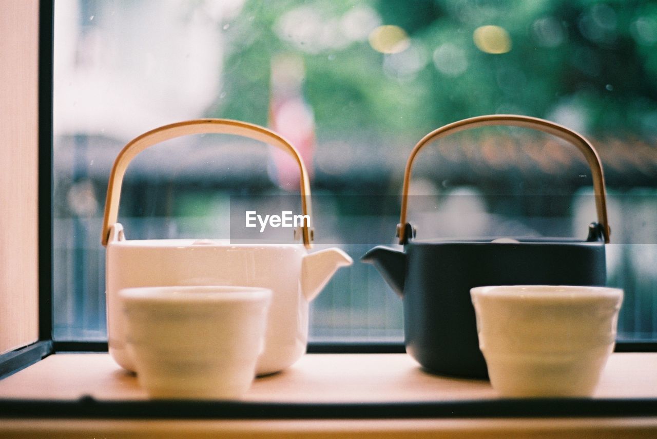 Close-up of cups and tea kettles in tray against window