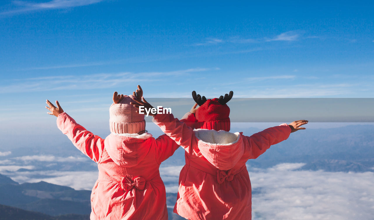 Rear view of siblings with arms outstretched standing against sky