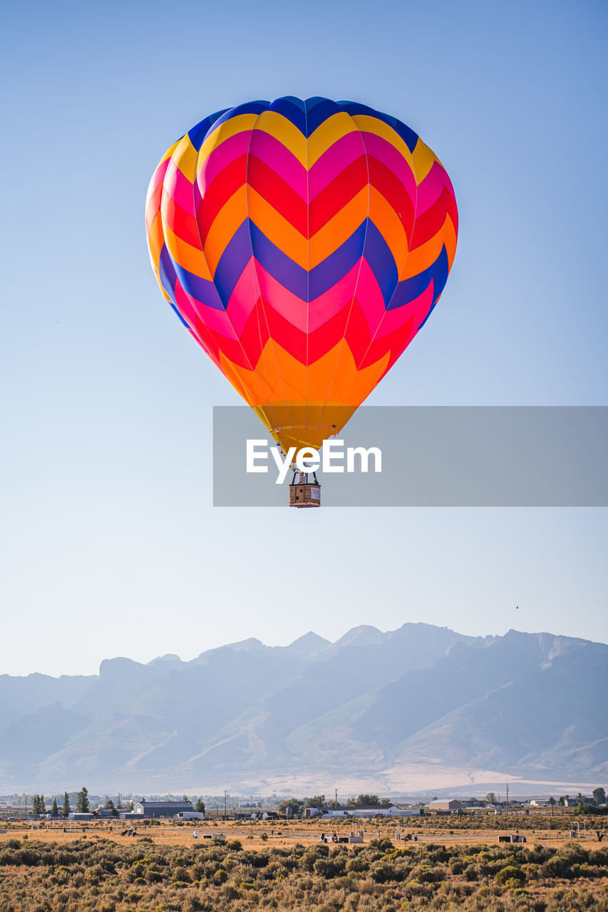 Colorful orange and blue hot air balloon flying above a mountain range desert landscape in nevada