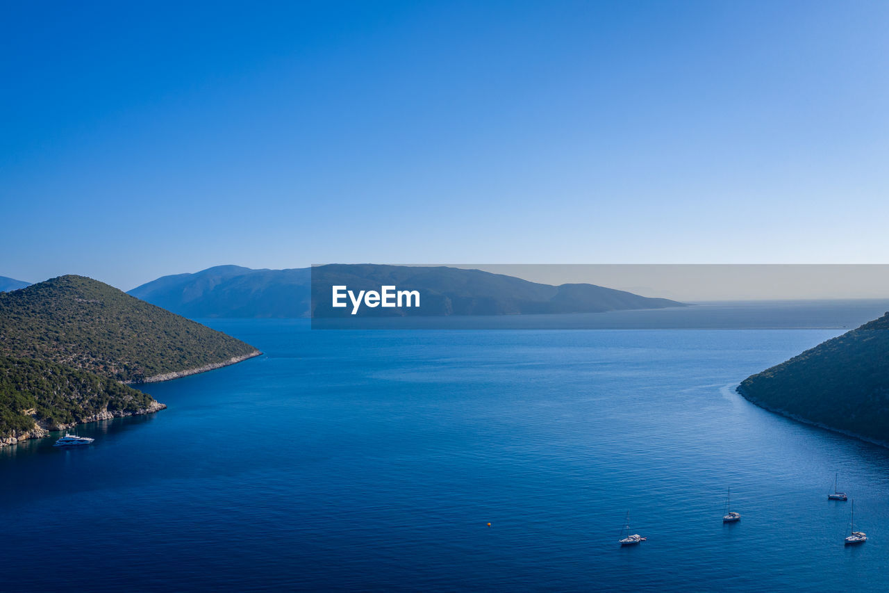 Scenic view of sea and mountains against clear blue sky