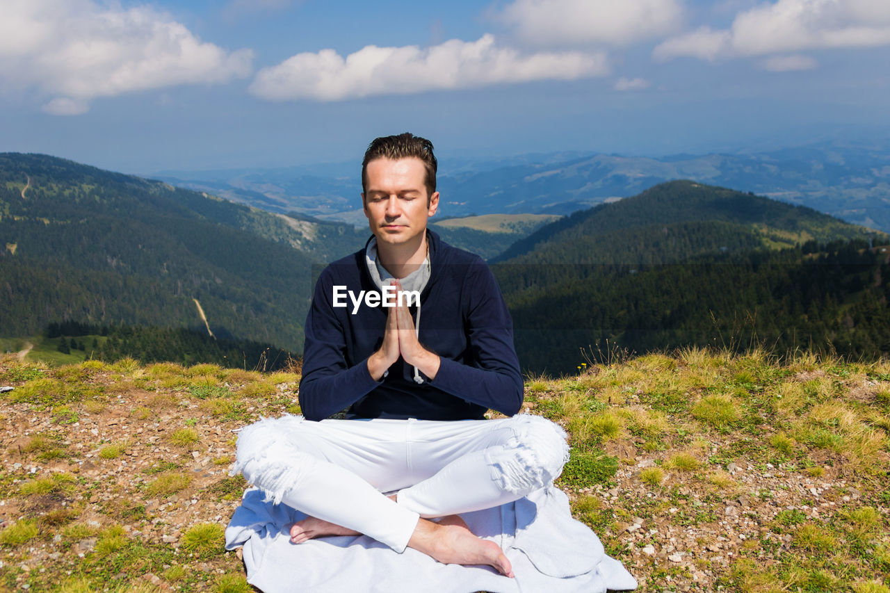 Peaceful man meditating in namaste pose on a meadow.