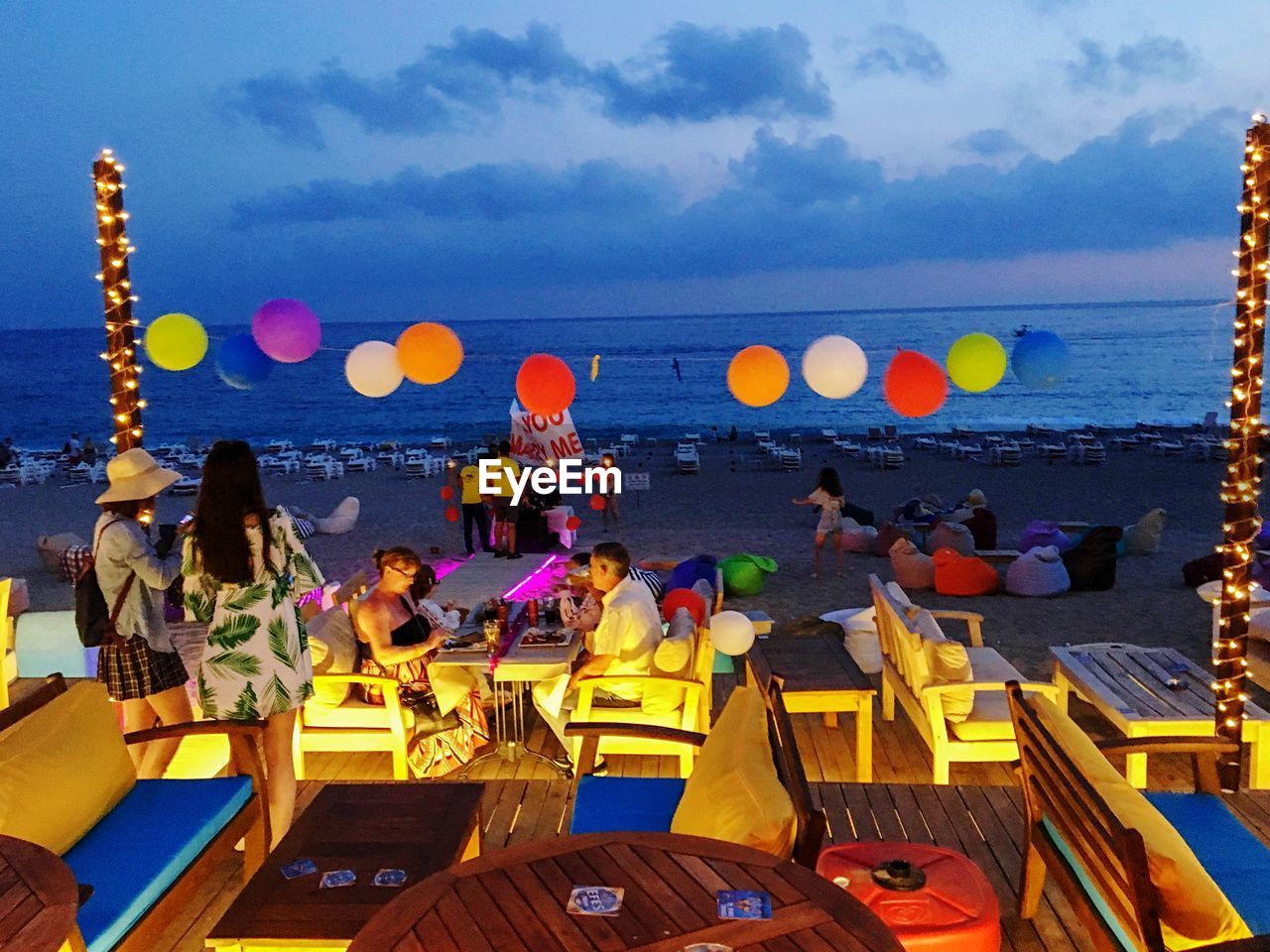 PEOPLE SITTING AT BEACH AGAINST SKY