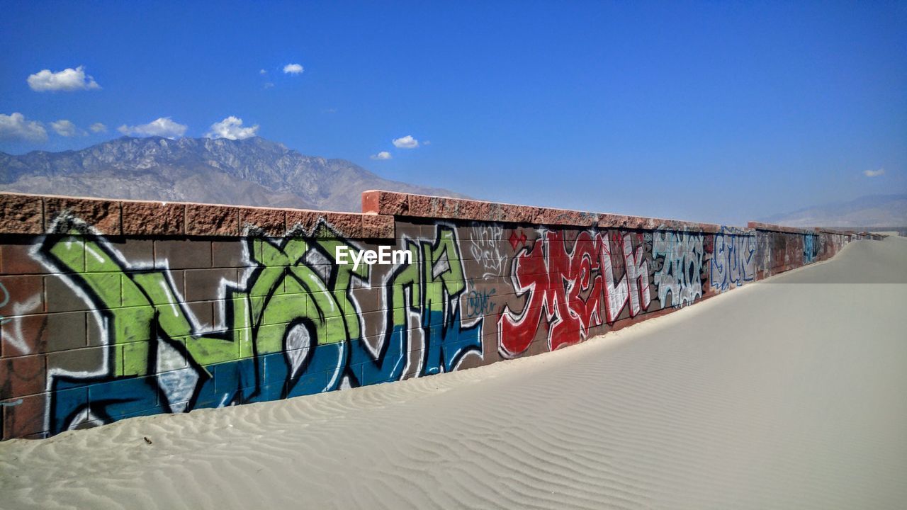 Colorful graffiti wall by sandy beach against sky