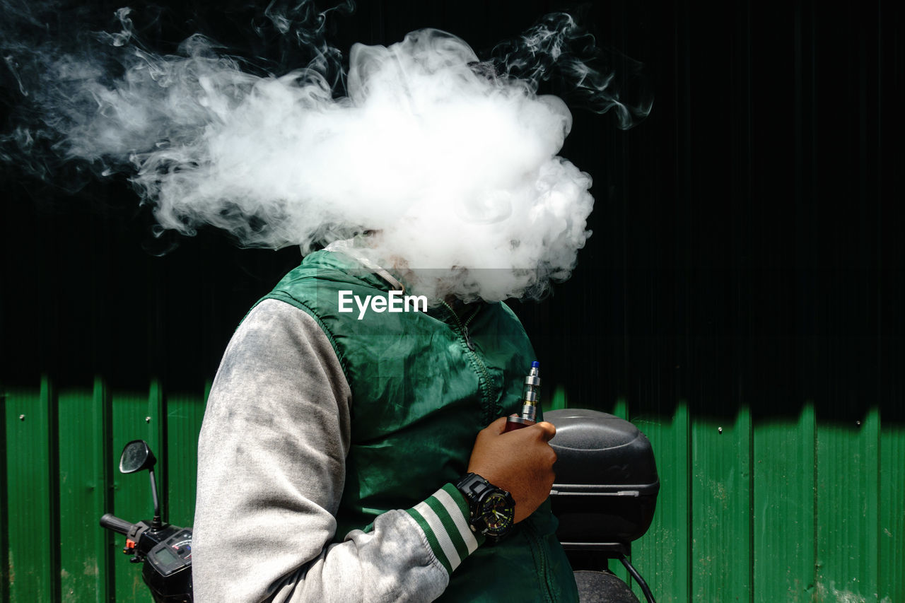 Man holding electronic cigarette while face covered with smoke