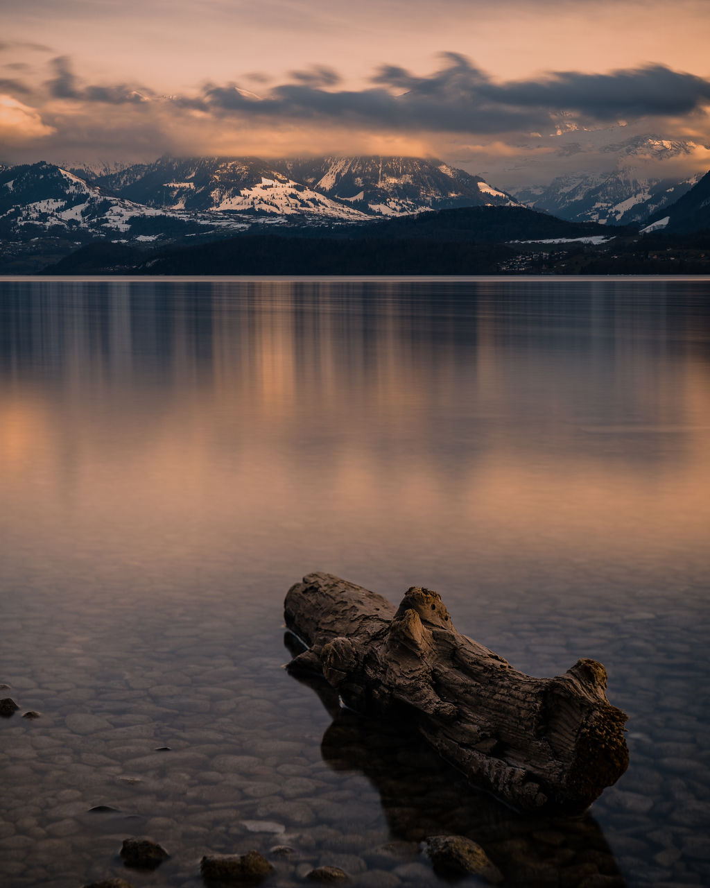 Scenic view of lake by snowcapped mountains against sky during sunset