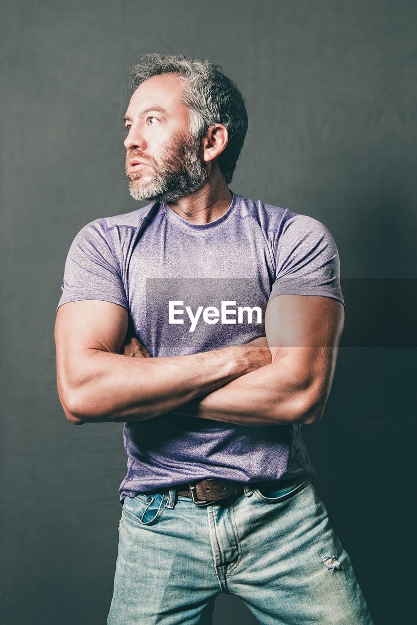 Confident man with arms crossed looking away against wall