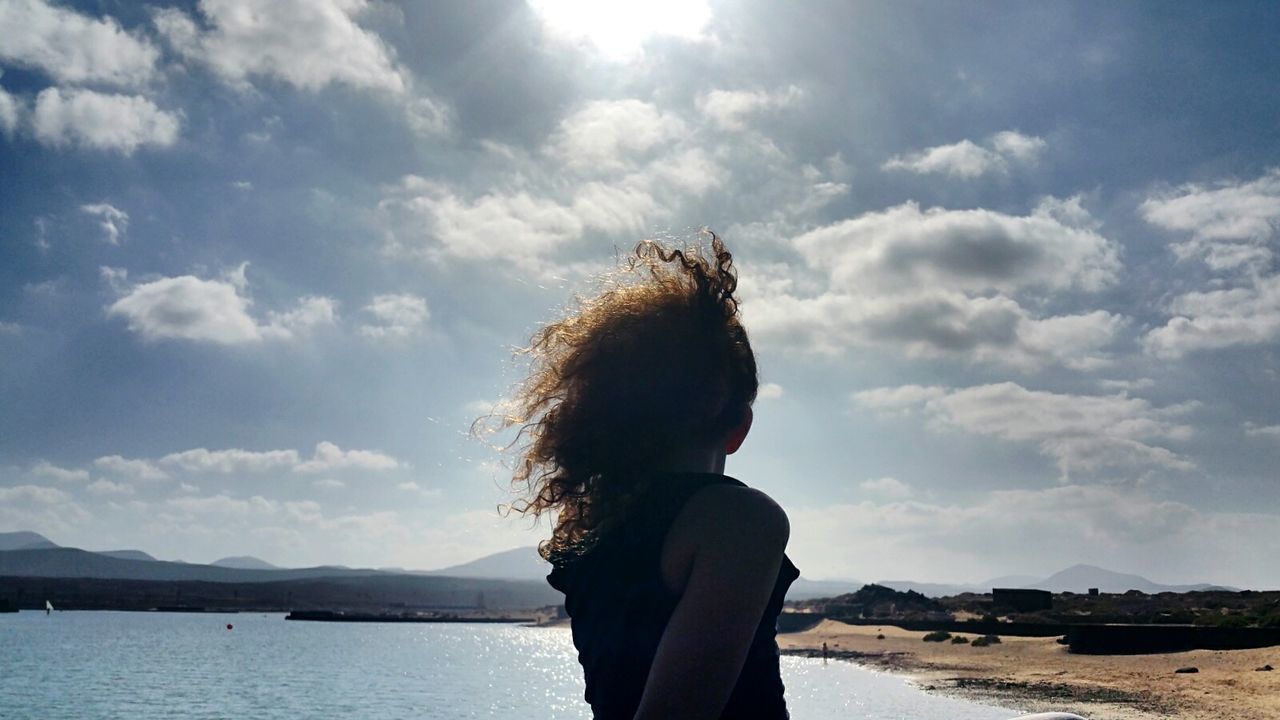 Girl on lakeshore against cloudy sky