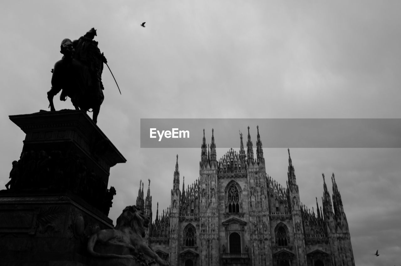 Low angle view of silhouette statue by milan cathedral against sky at dusk