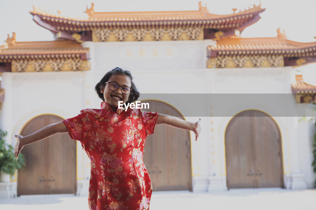 Portrait of cheerful girl with arms outstretched against temple