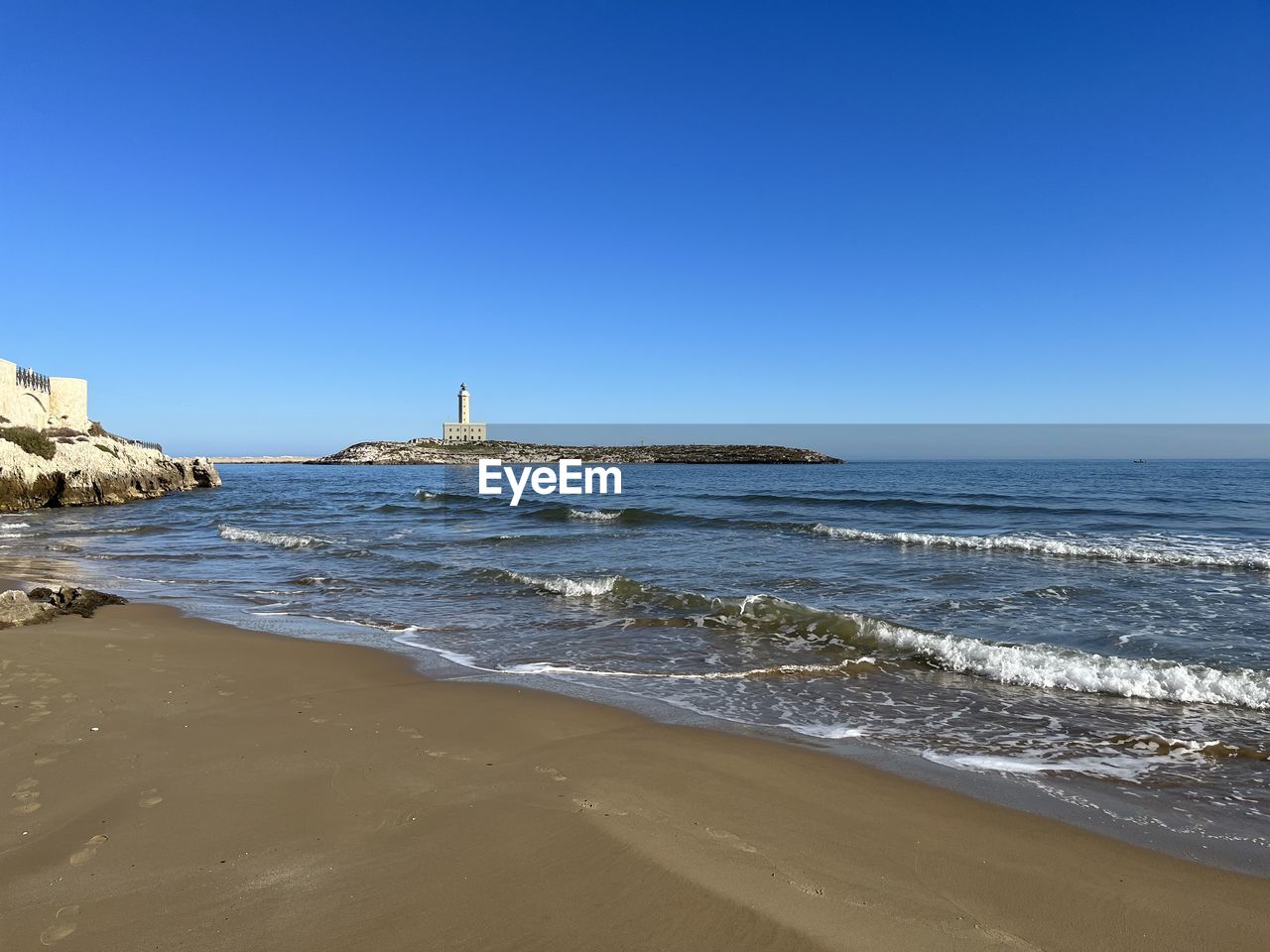 sea, water, land, beach, sky, body of water, wave, nature, shore, ocean, sand, scenics - nature, lighthouse, clear sky, architecture, coast, blue, travel destinations, beauty in nature, horizon, tower, travel, motion, built structure, wind wave, coastline, building exterior, environment, no people, horizon over water, guidance, building, day, water's edge, vacation, sunny, outdoors, tranquility, tourism, copy space, water sports, landscape, tranquil scene, trip, holiday, breakwater, sports, sunlight