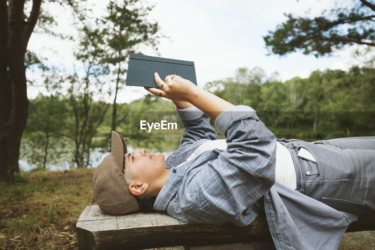 Young woman reading book while lying on wooden bench