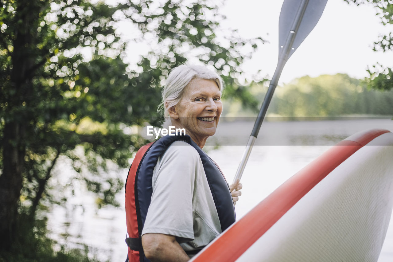 Portrait of happy senior woman holding paddleboard and oar