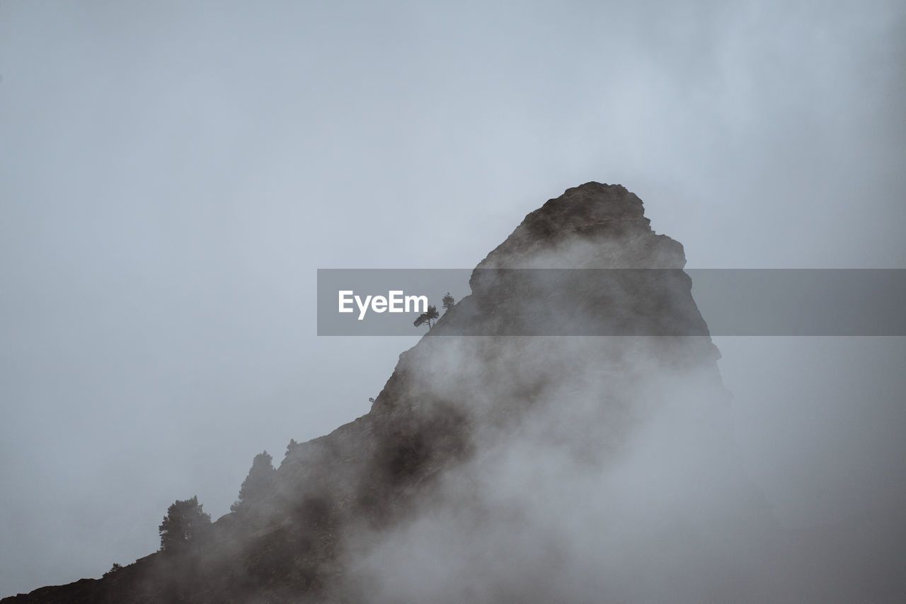 Low angle view of smoke emitting from rock against sky