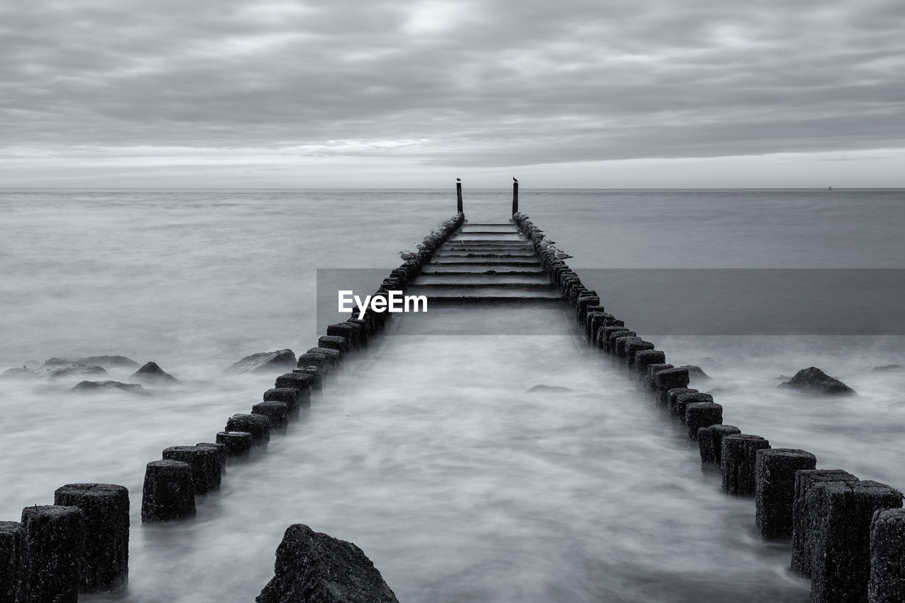 Wooden posts in sea against sky