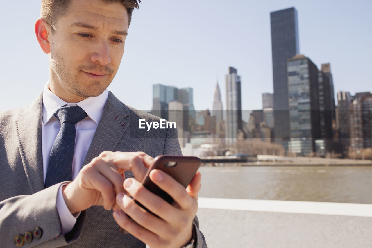 Portrait of a young businessman using his smartphone on a rooftop overlooking the city