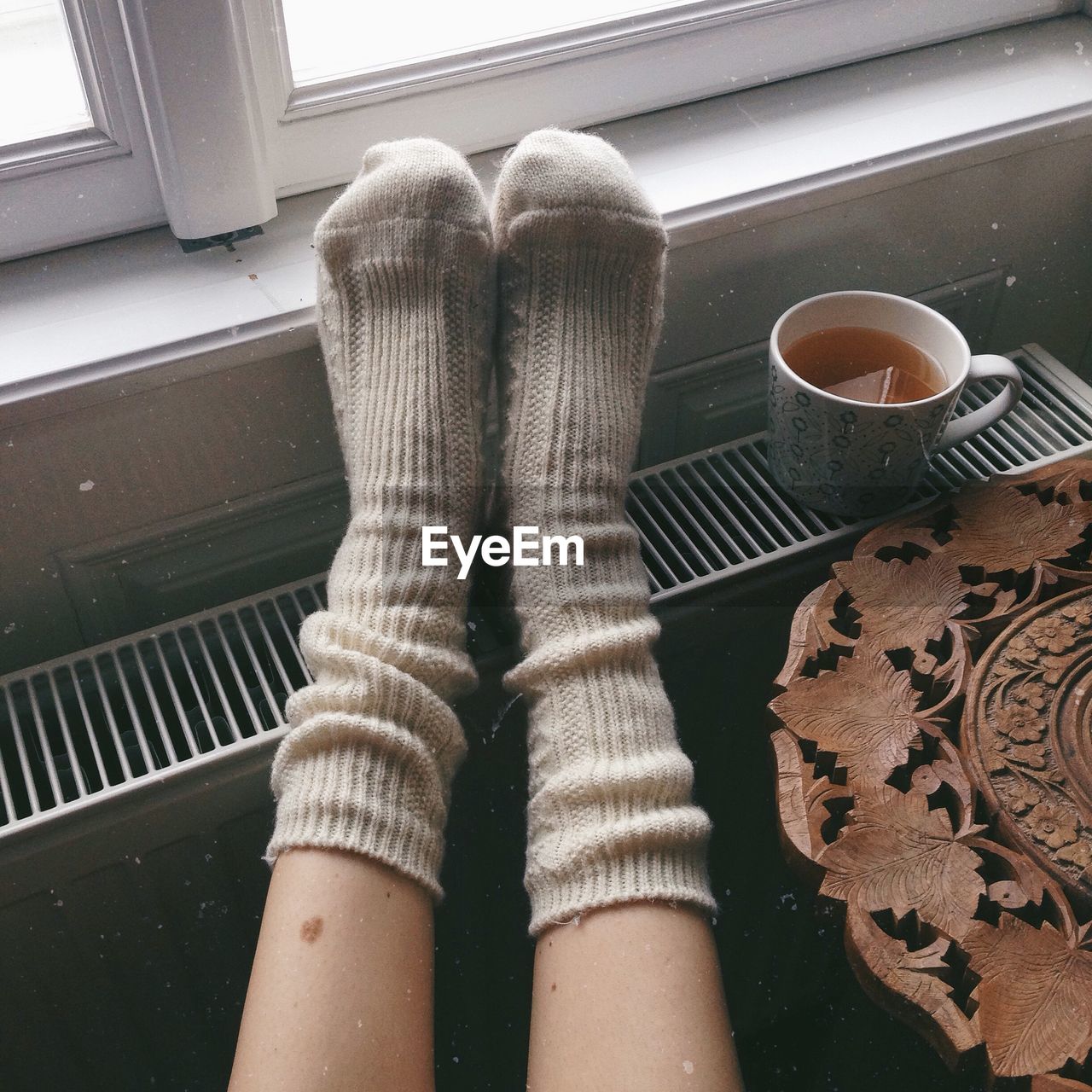 Low section of person wearing socks by tea cup on radiator at home