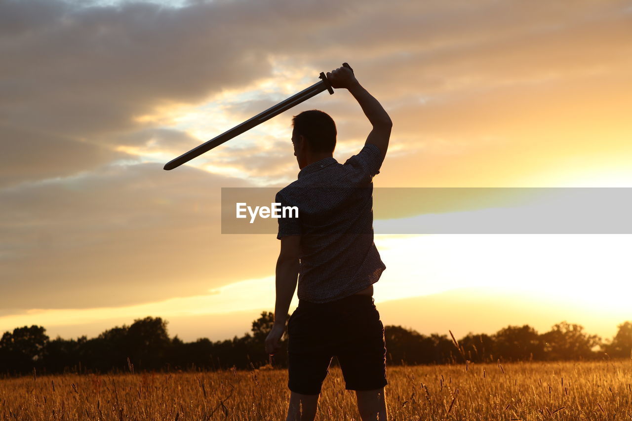 REAR VIEW OF MAN STANDING ON FIELD
