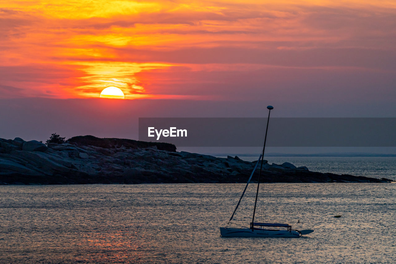 Isolated sailboat as the sun sets beyond clouds in the distance.