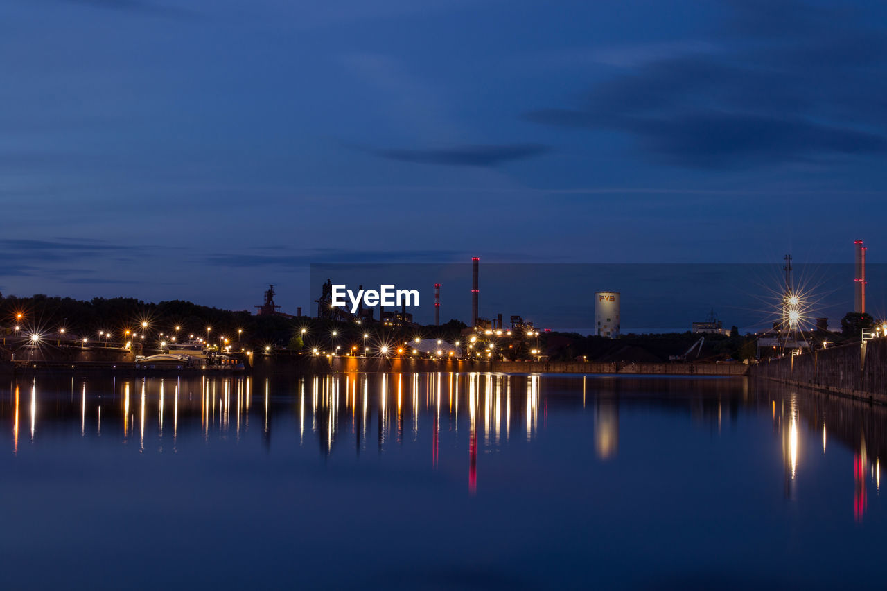 ILLUMINATED BUILDINGS BY LAKE AGAINST SKY AT NIGHT