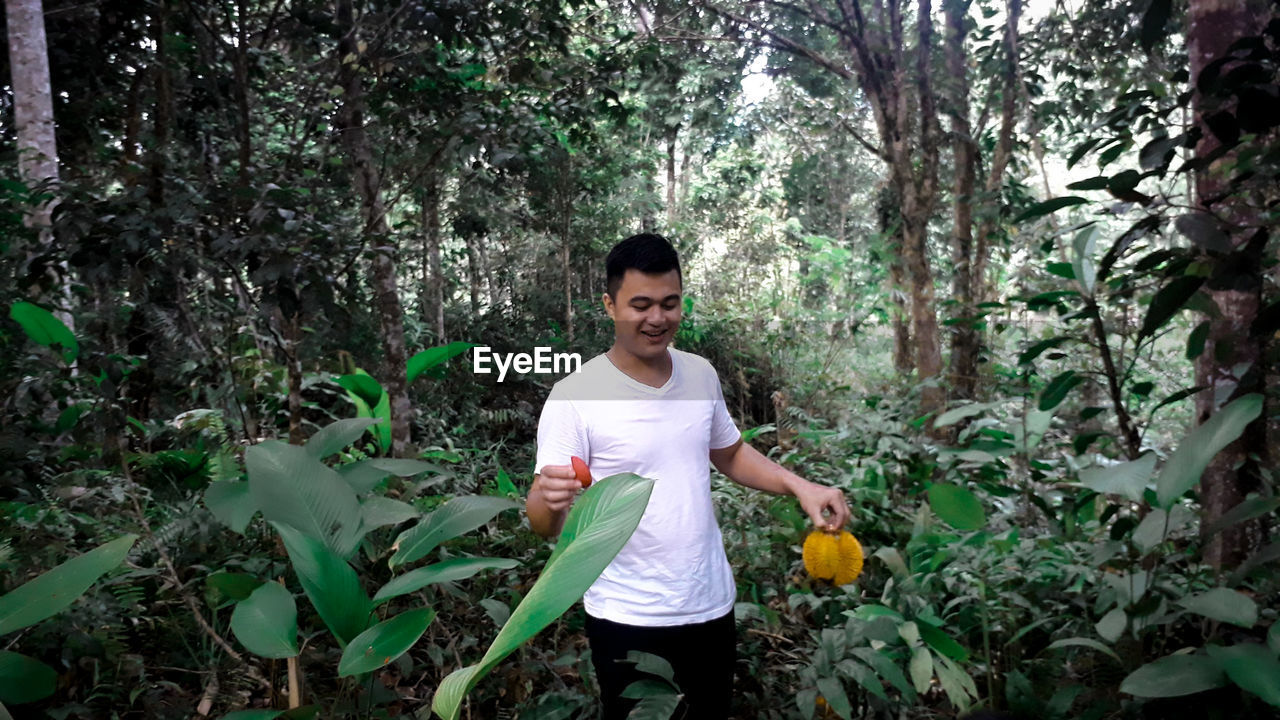 PORTRAIT OF YOUNG MAN STANDING BY PLANTS