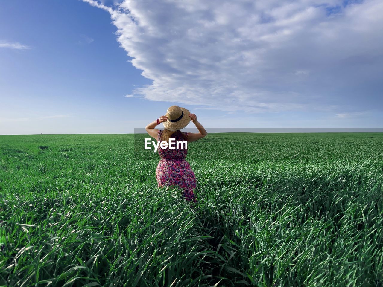 Rear view of woman wearing dress and hat in a field of green wheat