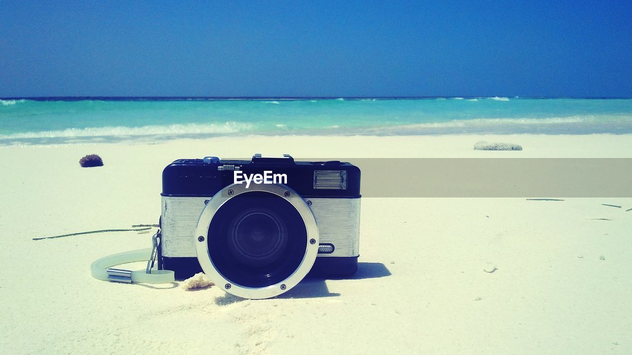 Camera on beach by sea against sky