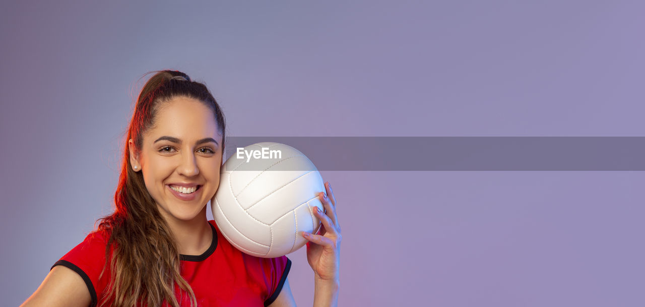 PORTRAIT OF A SMILING YOUNG WOMAN AGAINST WALL