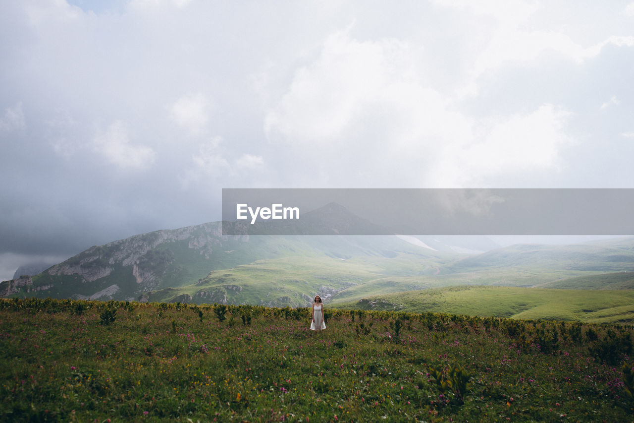 Woman sanding on field against mountains and sky