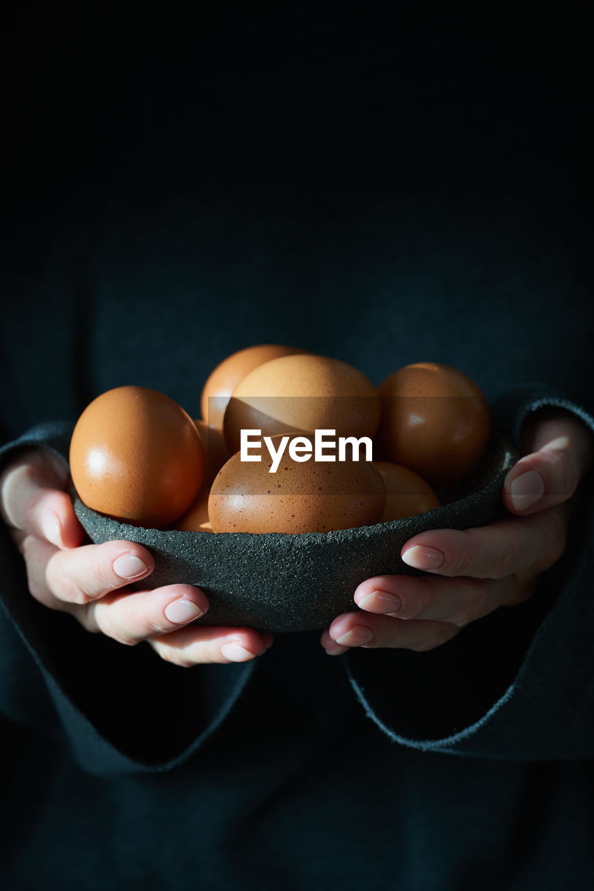 Unusual easter on a dark background. a bowl of brown eggs with hands. darkness, rays of sunlight