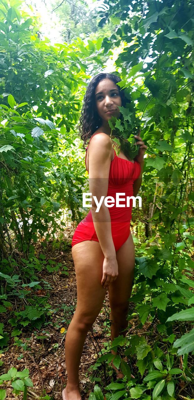 YOUNG WOMAN LOOKING DOWN WHILE STANDING BY PLANTS