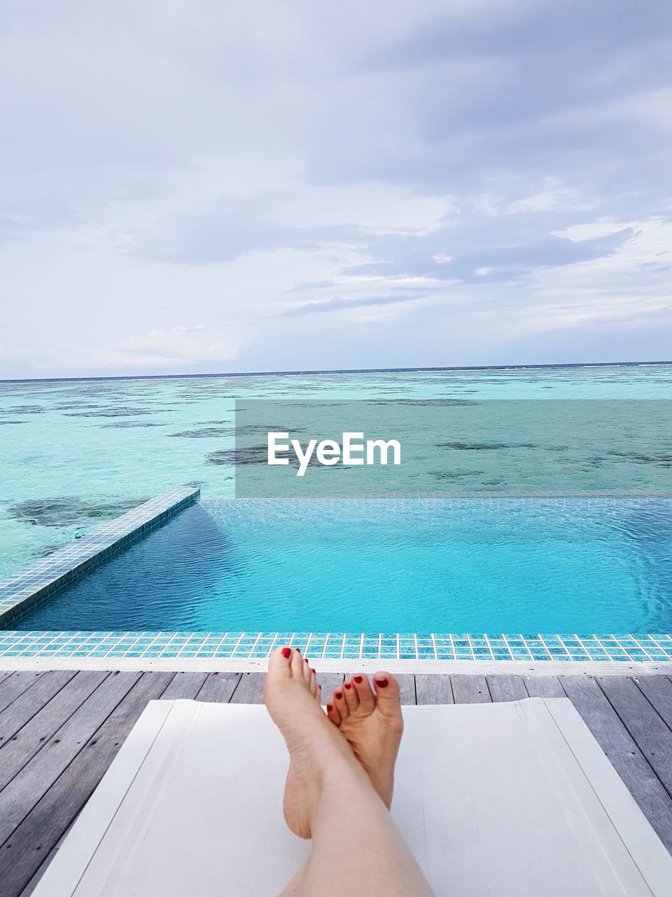 Low section of woman relaxing by infinity pool against sky