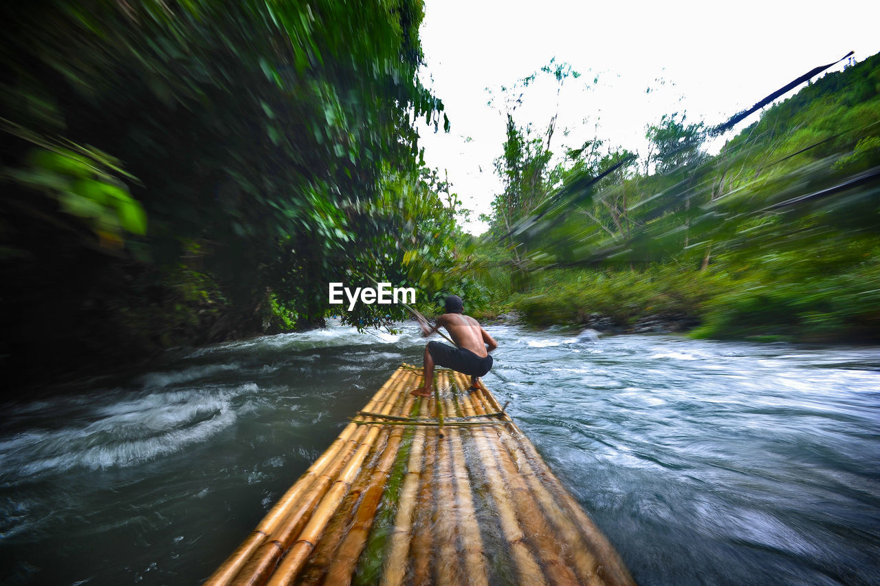 Rear view of man sailing wooden raft in river