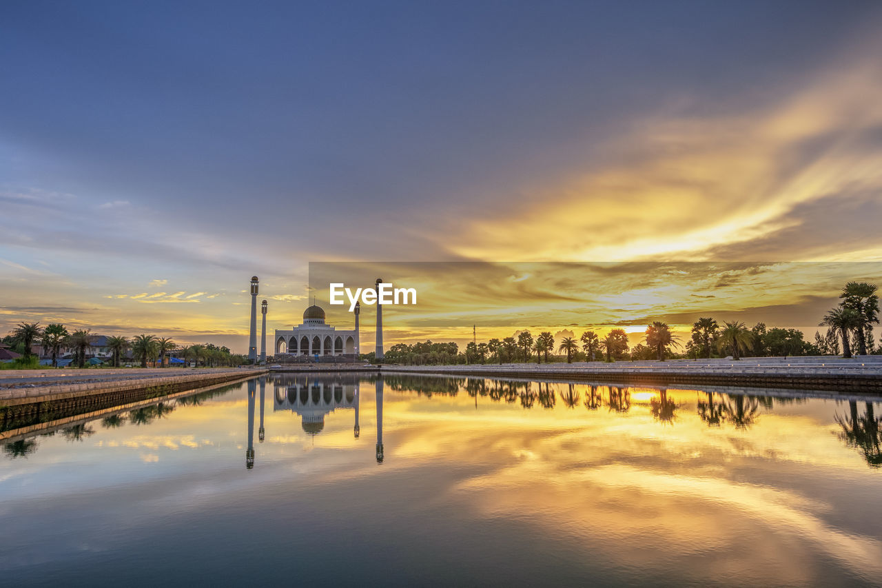 Reflection of mosque in lake against sky during sunset