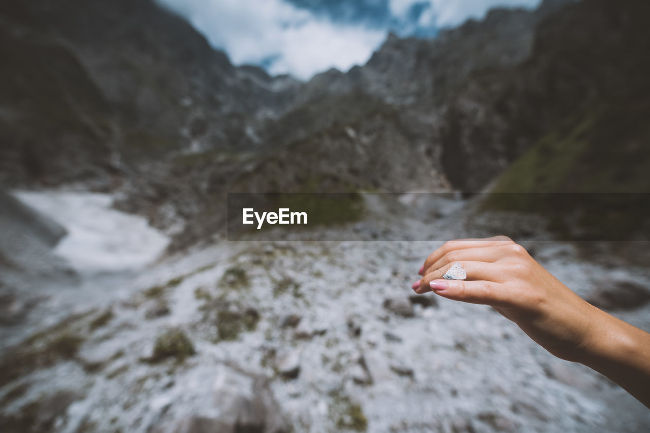 Cropped hand of woman with insect against mountains