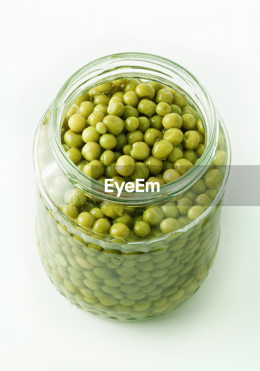 High angle view of green peas in jar over white background