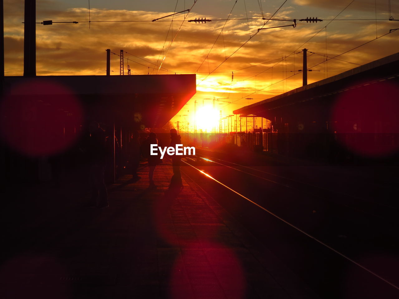 People at railroad station against sky during sunset