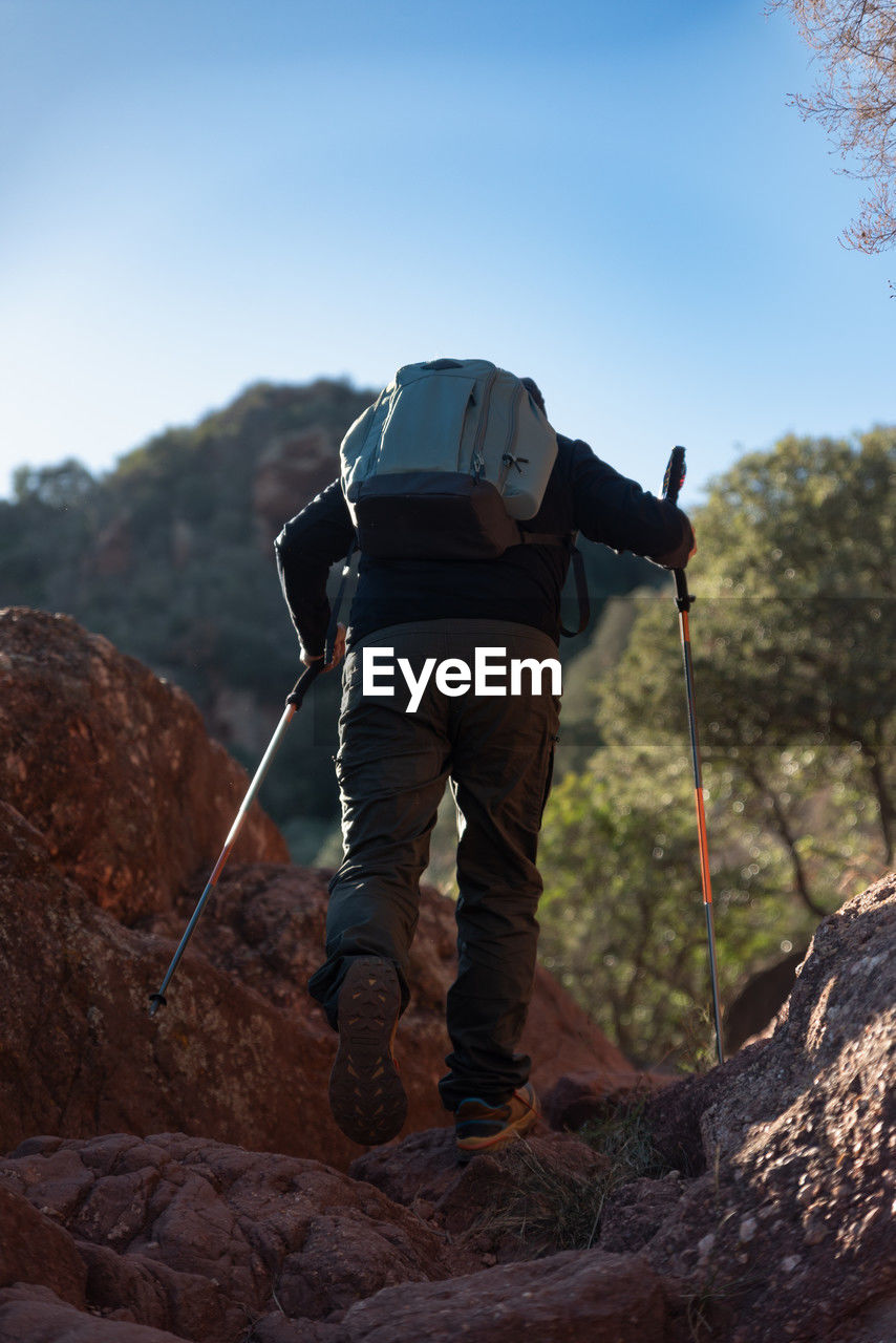 Middle-aged man climbs the mountain in the garraf natural park, supported by hiking poles.