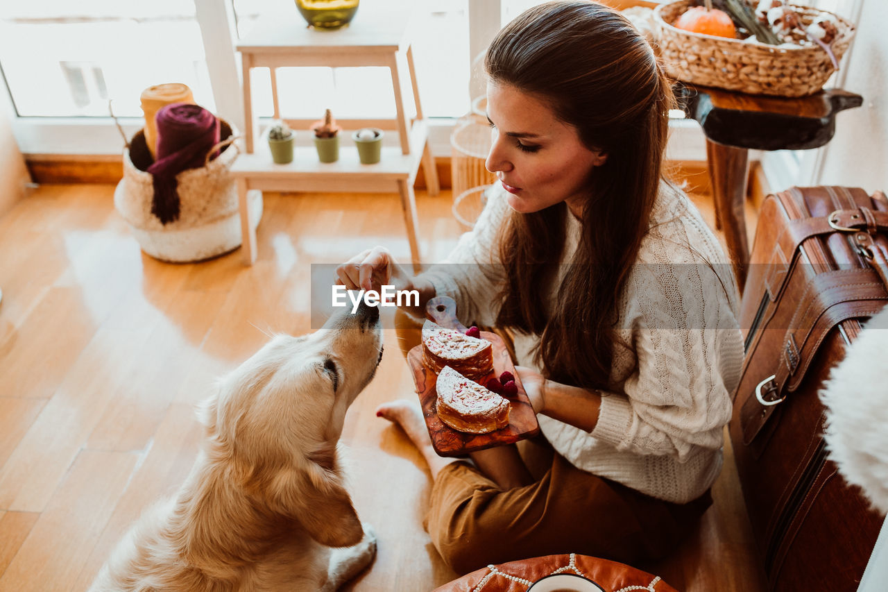 High angle view of woman feeding dog while sitting at home