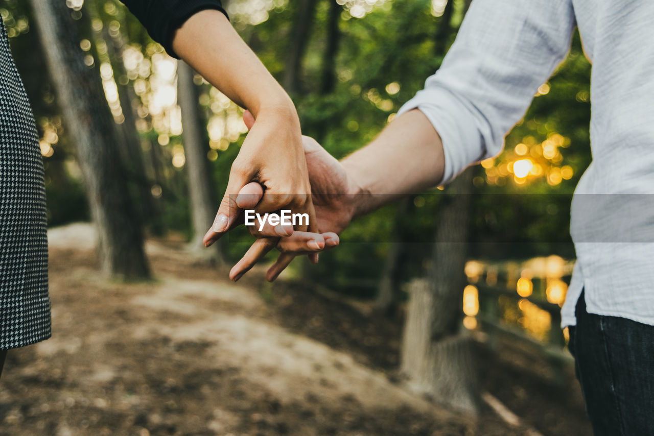 MIDSECTION OF MAN AND WOMAN HOLDING HANDS OUTDOORS