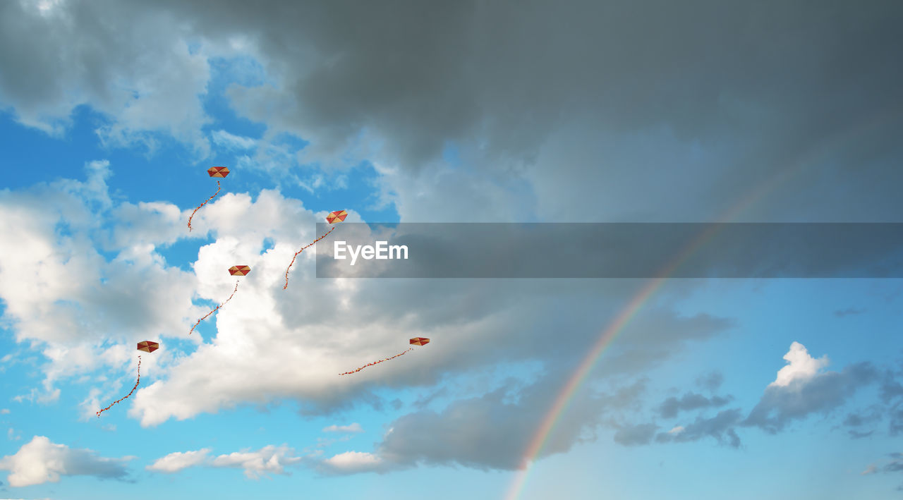 Flying kites in a sky with clouds and a rainbow