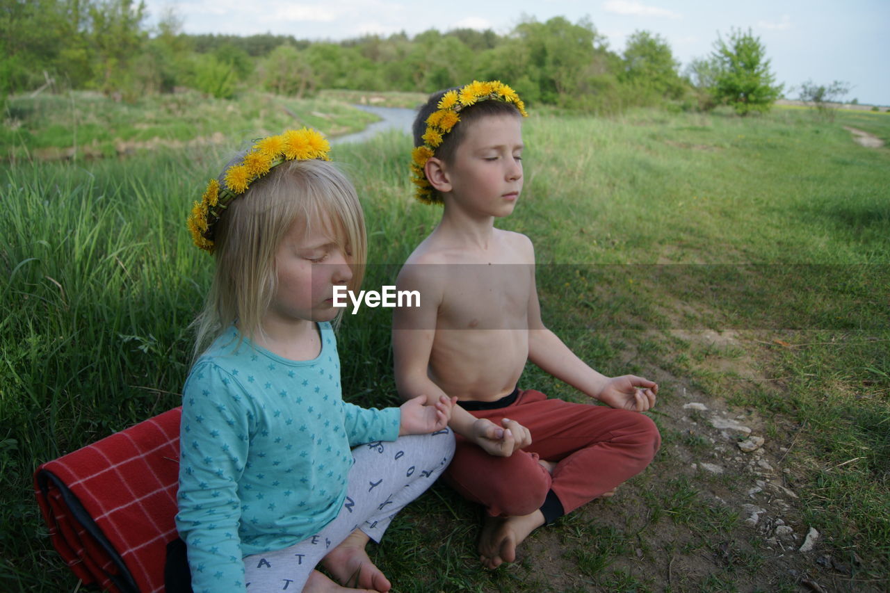 Friends with eyes closed wearing flowers while meditating on field