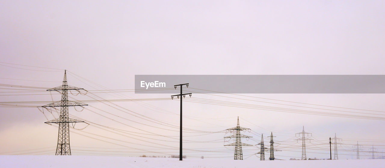 Low angle view of electricity pylons against clear sky