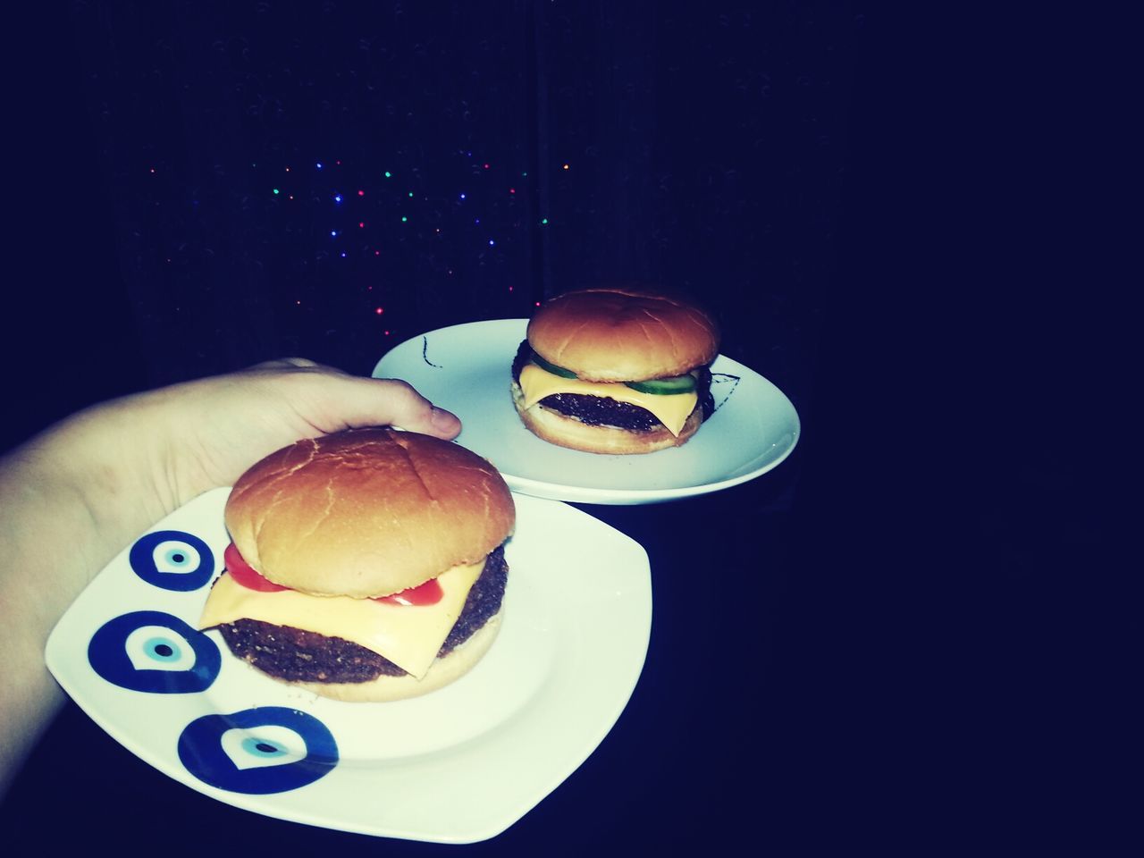 Cropped image of hand holding cheeseburgers in plates