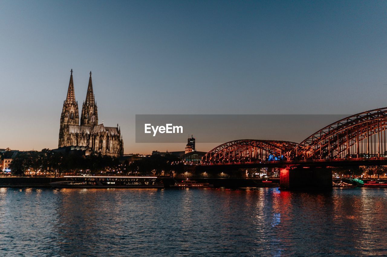 Bridge over river in city against sky at dusk