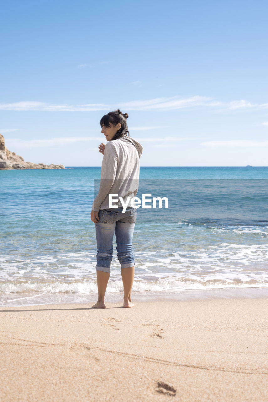 Rear view of a barefoot woman standing on seashore