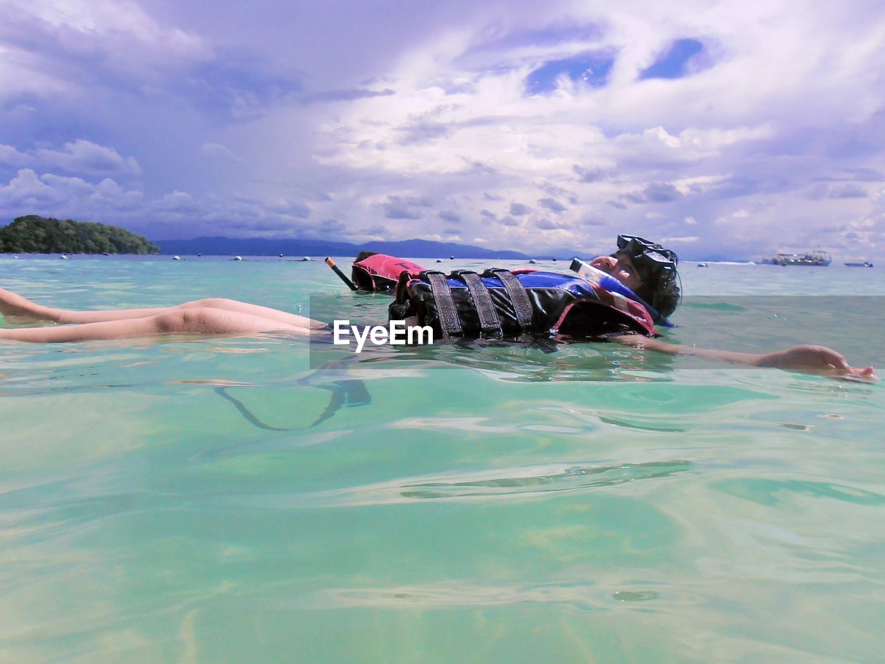 Side view of woman floating on sea against cloudy sky at beach