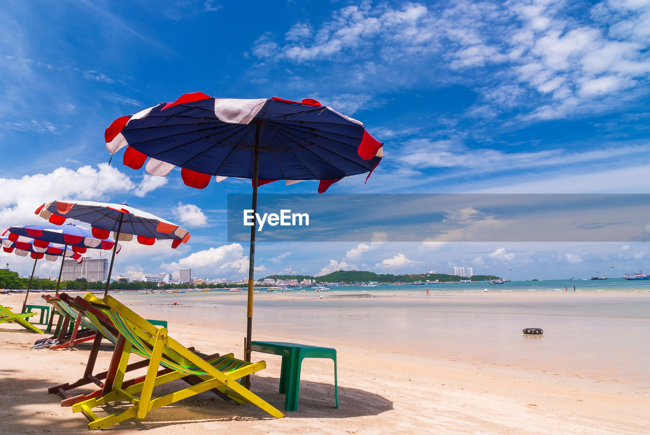 Deck chairs and parasols on shore at beach against sky